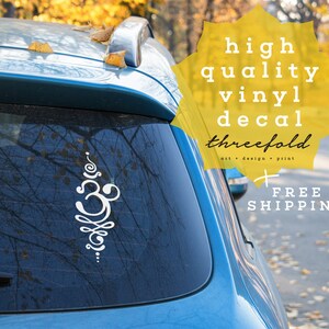 May include: White vinyl decal of an Om symbol on a blue car with the text "high quality vinyl decal threefold art + design + print FREE SHIPPING" in yellow.