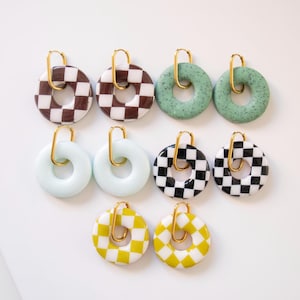 Peut inclure: Un ensemble de huit boucles d'oreilles créoles dorées avec des breloques en céramique en forme de beignets de différentes couleurs. Les breloques ont un motif à carreaux en brun et blanc, vert et blanc, noir et blanc, et jaune et blanc.