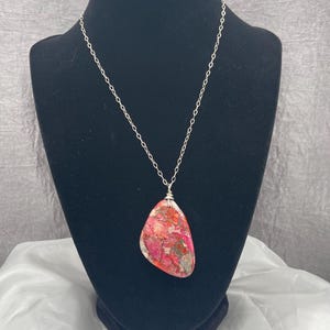 May include: A silver chain necklace with a large, pink, white, and brown stone pendant. The stone has a unique, marbled pattern.
