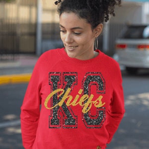 Op de afbeelding: Rood sweatshirt met een zwart en gouden glitterontwerp met de tekst "KC Chiefs".