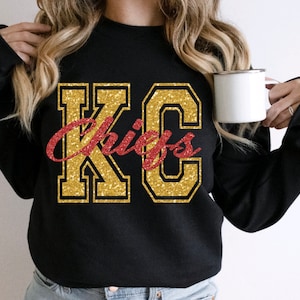 Op de afbeelding: Zwart sweatshirt met gouden glitter "KC Chiefs" belettering.