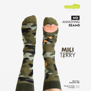 Pode incluir: Meias de camuflagem verde-oliva com um desenho de rosto de desenho animado. As meias apresentam o texto "NO ANNOYING SEAMS" e "MILI TERRY". São rotuladas como "Oeko-Tex Standard 100" e "Design & Made in Europe".