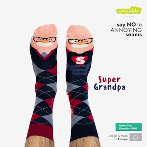 Pode incluir: Um par de meias azuis e vermelhas com padrão de argyle, com uma imagem de desenho animado de um avô sorridente usando óculos. As meias têm o texto "Super Grandpa" e "say NO to ANNOYING seams". As meias são feitas com materiais certificados Oeko-Tex Standard 100 e são projetadas e fabricadas na Europa.