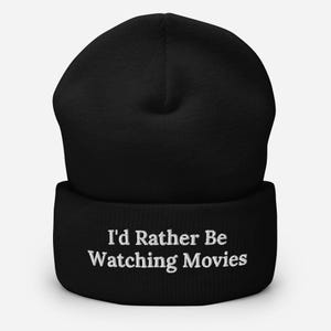 Peut inclure: Bonnet noir avec le texte brodé en blanc "I'd Rather Be Watching Movies". Le bonnet est fait d'une matière tricotée douce et possède un revers. Un cadeau idéal pour les cinéphiles.