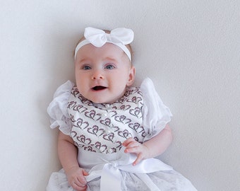 Festive baby dirndl made of cotton with a heart pattern in pink and green, with a lace apron.