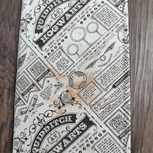 May include: A rectangular fabric panel featuring a black and white Quidditch at Hogwarts print with vintage-style typography, illustrations of a Golden Snitch, Quaffle, and broomsticks, alongside descriptive text blocks and house crests.