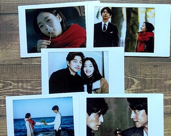May include: A collage of five Polaroid photos featuring a couple in various settings. The photos show the couple in a car, walking in a forest, standing on a beach, and looking at each other. The photos are arranged in a grid pattern.