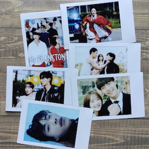 May include: A collection of six Polaroid photos featuring various scenes, including a couple in a car, a group of people, a couple in a park, a couple in a field, and a man lying down. The photos are all in a white frame.