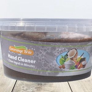 Puede incluir: Un recipiente de plástico transparente con un limpiador de manos marrón en su interior. La etiqueta dice "Cocorange Brite Hand Cleaner Clean Hands in Minutes". La etiqueta también presenta un gráfico de un coco, una manzana y otros ingredientes.