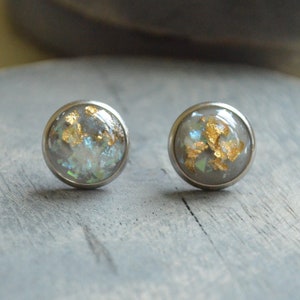 May include: A pair of silver stud earrings with a clear resin base and gold flakes embedded inside.