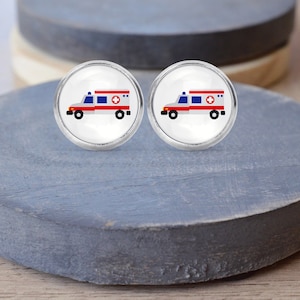 May include: A pair of silver-toned earrings with a white background and a red and blue cartoon ambulance image.