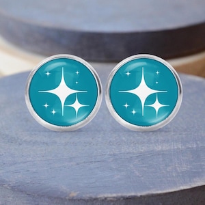 Peut inclure: Une paire de boucles d'oreilles rondes avec un fond turquoise et un motif d'éclat blanc. Les boucles d'oreilles ont une bordure en métal argenté. Les boucles d'oreilles sont présentées sur une surface bleue.