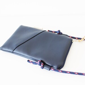 May include: A dark blue crossbody bag with a zipper closure and a rope strap with red and white accents.