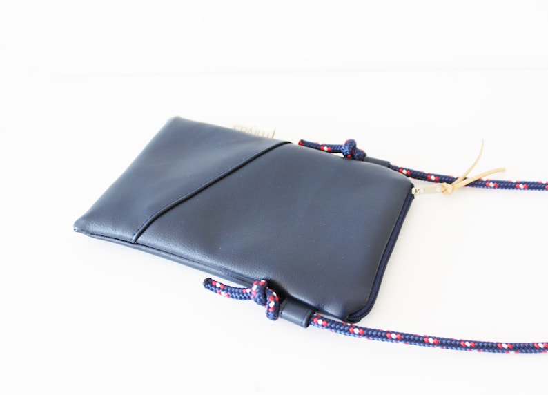 May include: A dark blue crossbody bag with a zipper closure and a rope strap with red and white accents.