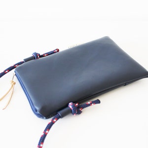 May include: A dark blue leather phone pouch with a zipper closure and a red and white rope strap.