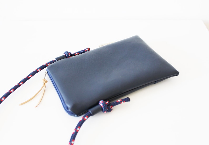 May include: A dark blue leather phone pouch with a zipper closure and a red and white rope strap.