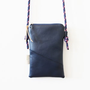 May include: A small navy blue leather crossbody bag with a zipper closure and a red, white, and blue rope strap. The bag has a label that says "miyas".
