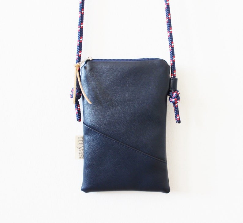 May include: A small navy blue leather crossbody bag with a zipper closure and a red, white, and blue rope strap. The bag has a label that says "miyas".