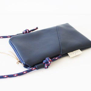 May include: A dark blue crossbody phone bag with a zipper closure and a red, white, and blue rope strap. The bag has a small label that says "miyas".