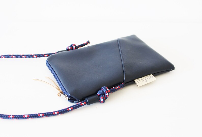 May include: A dark blue crossbody phone bag with a zipper closure and a red, white, and blue rope strap. The bag has a small label that says "miyas".
