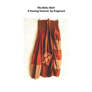 Puede incluir: Una falda larga de retazos marrones con un cinturón de tela marrón. La falda está colgada de una percha contra una pared blanca. El texto "The Boho Skirt" y "A Sewing Tutorial by Priganart" está impreso sobre la falda.