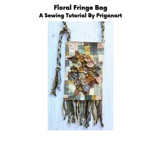 Może przedstawiać: Torebka z frędzlami w kwiatowym wzorze, z patchworkowym wzorem i plecionym paskiem. Torebka jest ozdobiona kwiatami z tkaniny w odcieniach brązu, beżu i zieleni. Torebka ma frędzlową lamówkę.