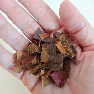 May include: A handful of fabric scraps in various shades of brown, red, and orange. The scraps are small and irregular in shape, and they appear to be made of cotton.
