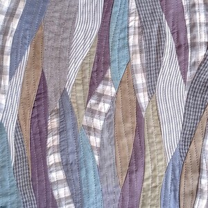 May include: A patchwork quilt with a wavy pattern of different colored fabrics. The fabrics are a mix of plaid, striped, and solid colors in shades of blue, brown, green, and purple.