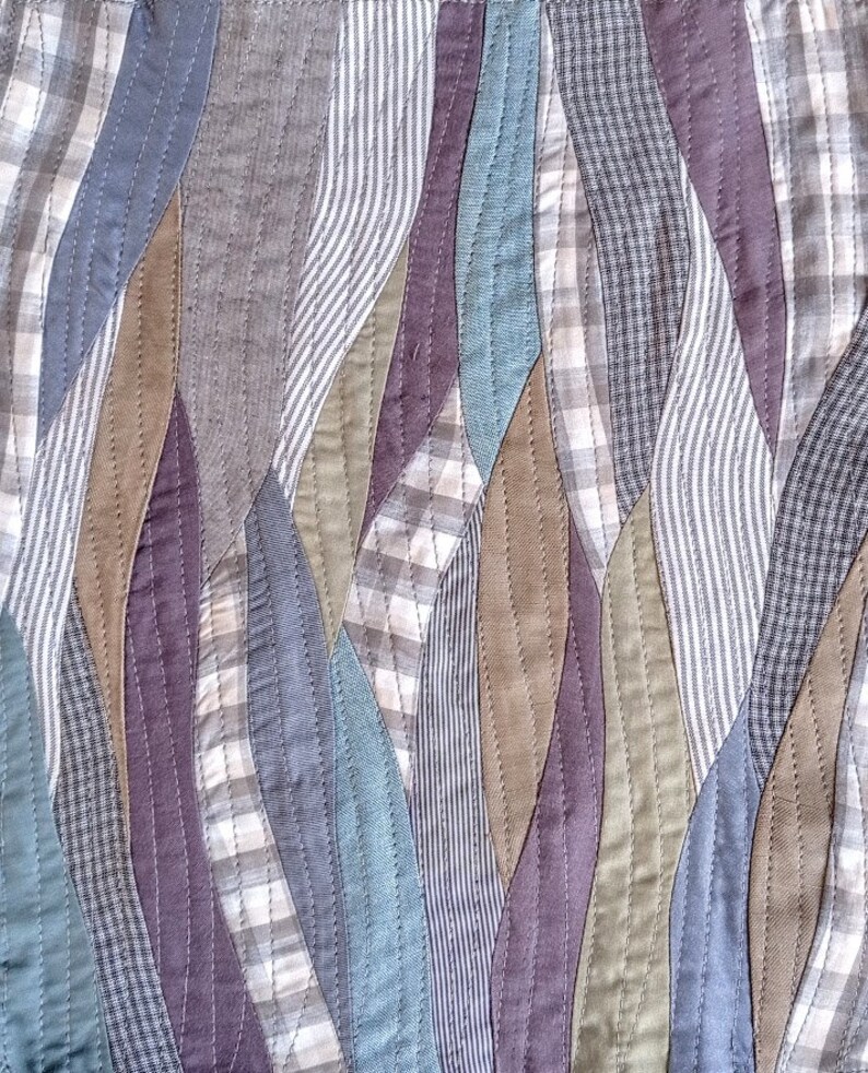 May include: A patchwork quilt with a wavy pattern of different colored fabrics. The fabrics are a mix of plaid, striped, and solid colors in shades of blue, brown, green, and purple.