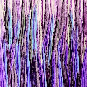 May include: A close-up of a fabric art piece with vertical strips of purple, blue, and white fabric. The fabric is sewn together to create a textured, abstract design.