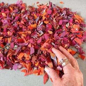 Pode incluir: Um monte de retalhos de tecido coloridos em tons de vermelho, laranja e roxo. Os retalhos est&atilde;o dispostos em um padr&atilde;o aleat&oacute;rio e s&atilde;o de v&aacute;rios tamanhos e formas.