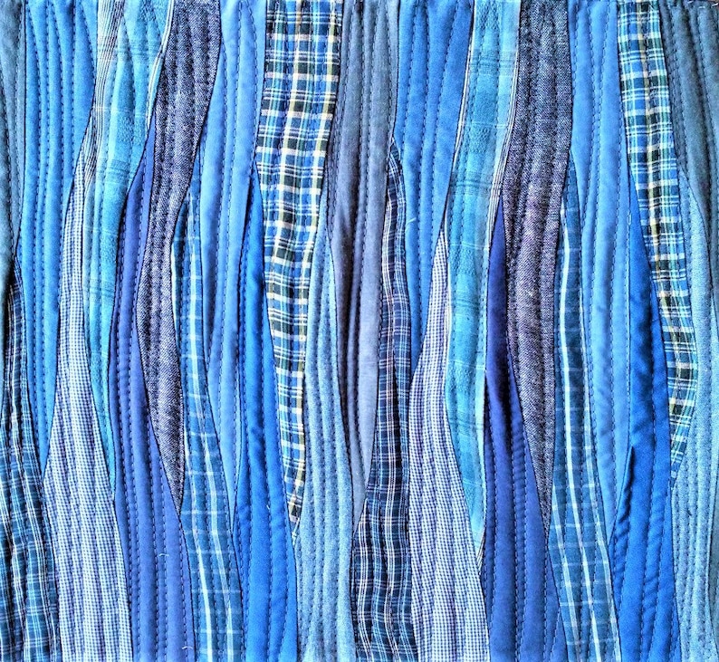 Puede incluir: Una colcha hecha de tiras de tela azul y blanca cosidas juntas en un patr&oacute;n ondulado. La tela es una mezcla de azul s&oacute;lido y cuadros.