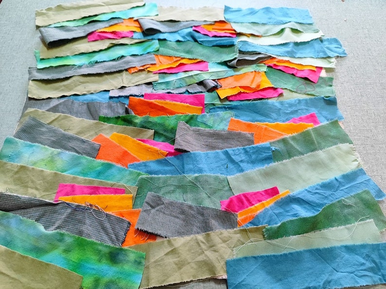 May include: A collection of fabric scraps in various shades of green, blue, orange, and pink. The fabric scraps are arranged in a layered pattern, creating a visual texture.