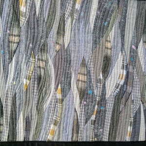 Puede incluir: Un primer plano de una colcha hecha de varios tonos de gris y marr&oacute;n. La tela est&aacute; cosida en un patr&oacute;n de hojas superpuestas, creando un aspecto texturizado y org&aacute;nico.