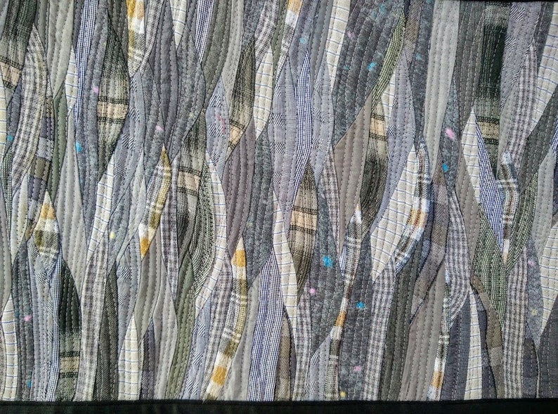 Puede incluir: Un primer plano de una colcha hecha de varios tonos de gris y marr&oacute;n. La tela est&aacute; cosida en un patr&oacute;n de hojas superpuestas, creando un aspecto texturizado y org&aacute;nico.