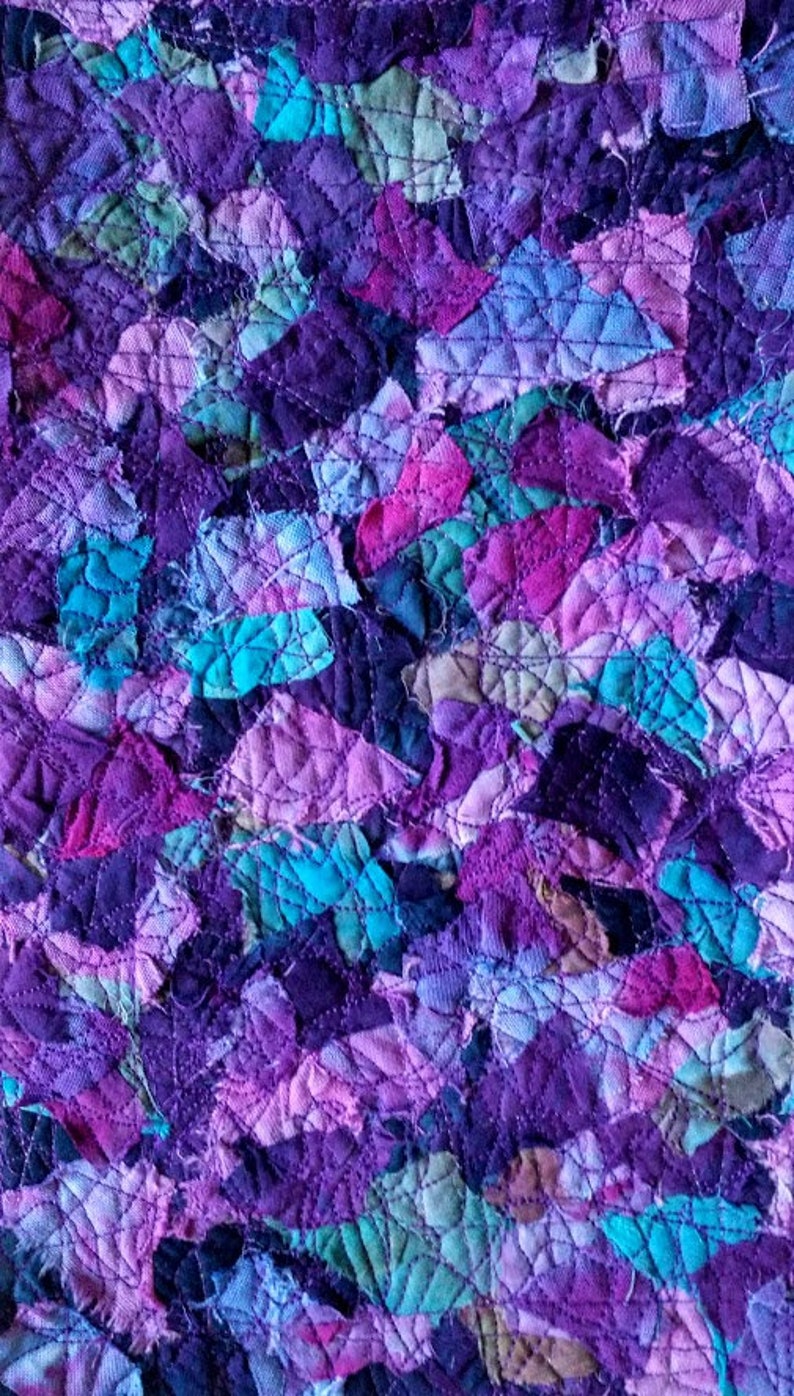 May include: Close-up of a quilted textile with a patchwork design. The fabric features a variety of purple, pink, teal, and green hues. The pieces are stitched together with a diamond pattern, creating a textured surface. The overall effect is a vibrant and colorful abstract design.