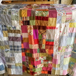 Puede incluir: Una colcha de retazos hecha con una variedad de telas en tonos de azul, verde, marr&oacute;n, rosa y blanco. La colcha est&aacute; hecha de cuadrados y rect&aacute;ngulos de diferentes tama&ntilde;os y patrones.