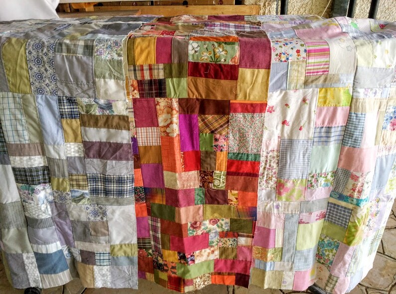 Puede incluir: Una colcha de retazos hecha con una variedad de telas en tonos de azul, verde, marr&oacute;n, rosa y blanco. La colcha est&aacute; hecha de cuadrados y rect&aacute;ngulos de diferentes tama&ntilde;os y patrones.