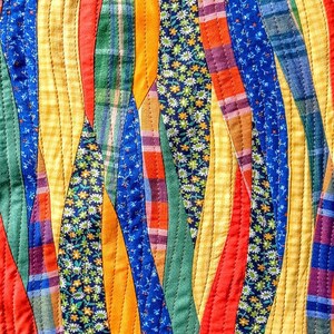 May include: A colorful quilt made of fabric scraps sewn together in a wavy pattern. The quilt features a variety of colors, including yellow, orange, red, green, blue, and purple. The fabric scraps are sewn together in a way that creates a flowing, organic design.
