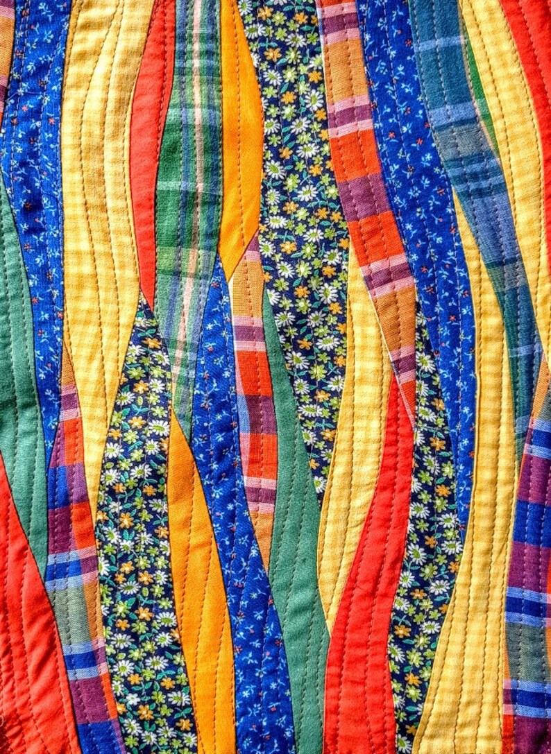 May include: A colorful quilt made of fabric scraps sewn together in a wavy pattern. The quilt features a variety of colors, including yellow, orange, red, green, blue, and purple. The fabric scraps are sewn together in a way that creates a flowing, organic design.