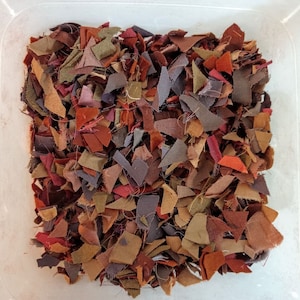 May include: A close-up of a container filled with small scraps of fabric in various shades of brown, red, and purple.