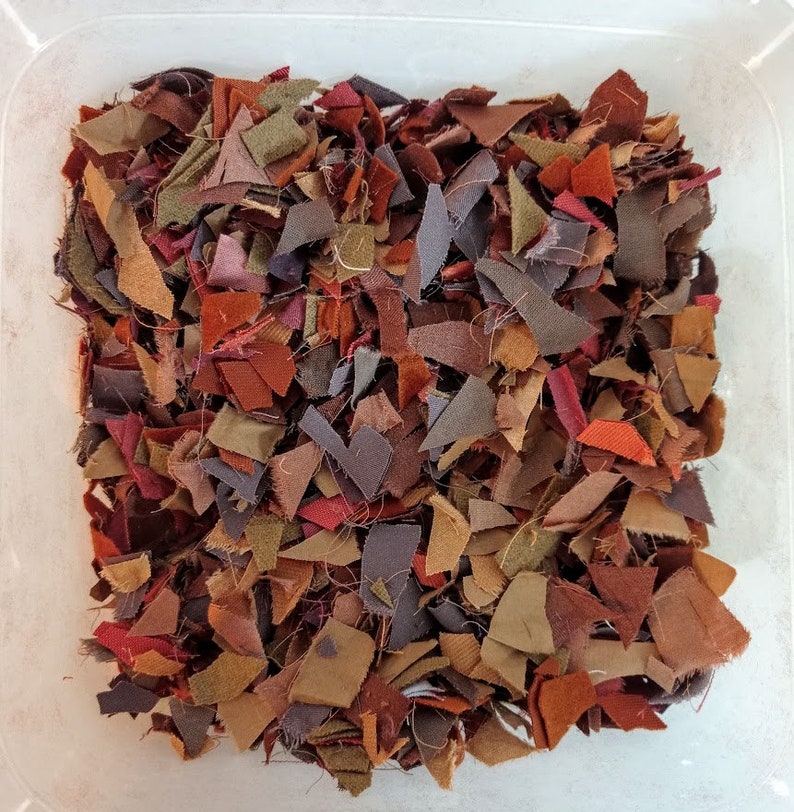 May include: A close-up of a container filled with small scraps of fabric in various shades of brown, red, and purple.