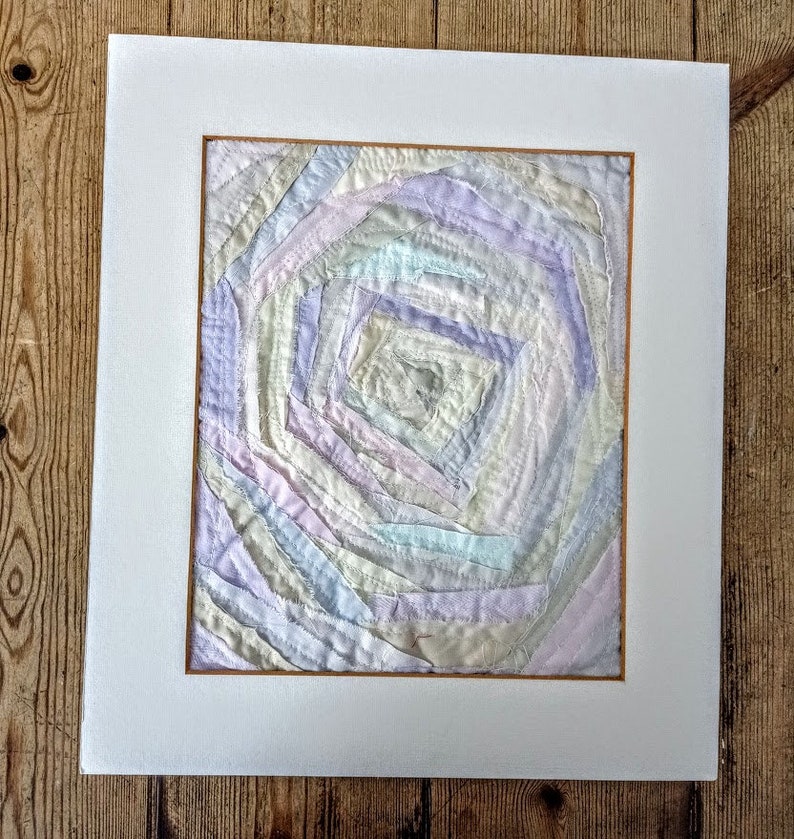 Pu&ograve; includere: Un'opera d'arte astratta incorniciata che presenta un motivo a spirale di ritagli di tessuto dai colori pastello. Il tessuto &egrave; sovrapposto e cucito per creare un effetto testurizzato e tridimensionale.