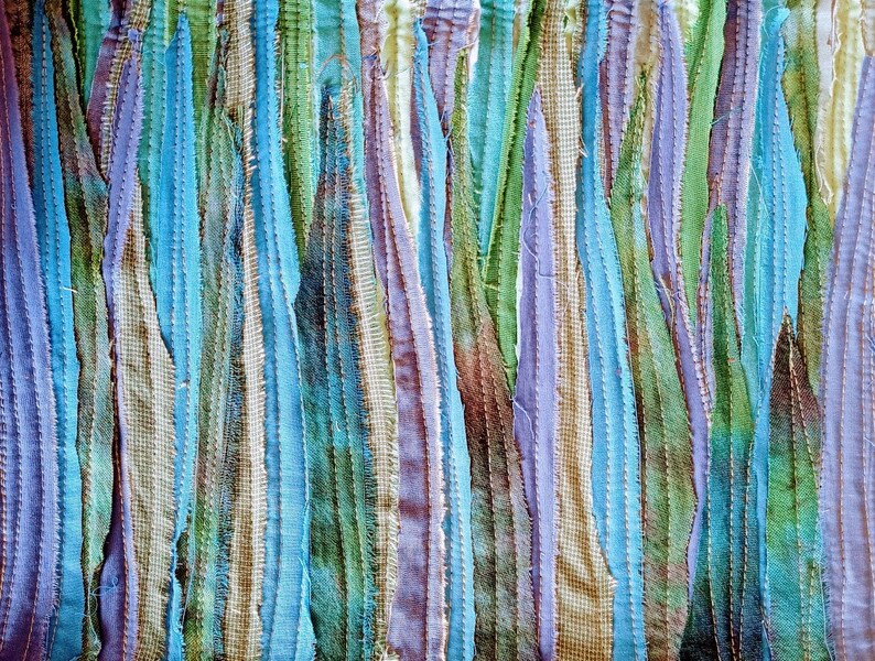 Puede incluir: Primer plano de una textura de tela con tiras verticales de tela en tonos de azul, verde, morado y marr&oacute;n. La tela est&aacute; cosida para crear un efecto de patchwork.