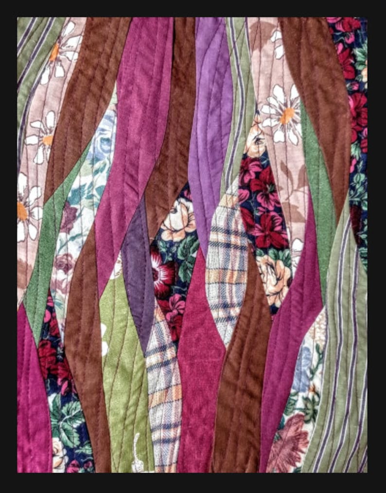 May include: A quilt made from assorted fabric scraps in shades of brown, purple, green, and red. The fabric is sewn together in a wavy pattern, creating a unique and textured design.
