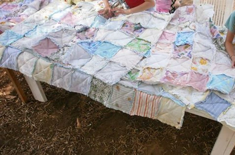 May include: A patchwork quilt made from a variety of fabrics in shades of pink, blue, and white. The quilt is made up of squares and rectangles, and the edges are frayed. The quilt is lying on a table.