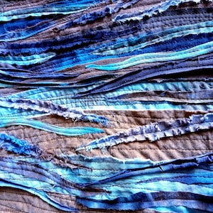 Pu&ograve; includere: Primo piano di una texture di tessuto realizzata con strisce di tessuto blu, turchese e marrone cucite insieme in un motivo ondulato.