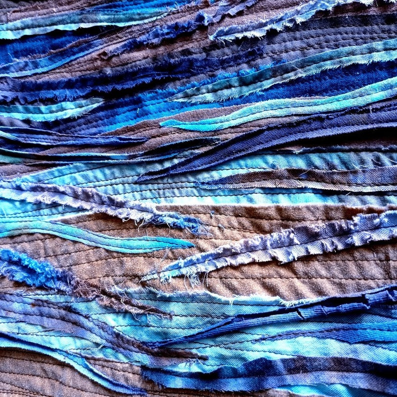 Pu&ograve; includere: Primo piano di una texture di tessuto realizzata con strisce di tessuto blu, turchese e marrone cucite insieme in un motivo ondulato.