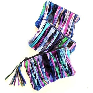 Puede incluir: Tres bolsas de tela coloridas con detalles de flecos. Las bolsas est&aacute;n hechas de tiras de tela en tonos azules, morados, rosas y verdes. Las bolsas tienen cierre de cremallera y un borla.