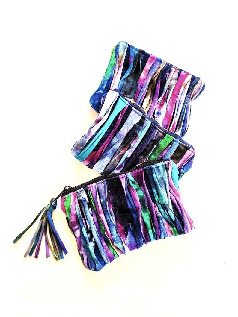 Puede incluir: Tres bolsas de tela coloridas con detalles de flecos. Las bolsas est&aacute;n hechas de tiras de tela en tonos azules, morados, rosas y verdes. Las bolsas tienen cierre de cremallera y un borla.